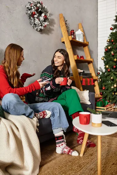 Girlfriends enjoy hot drinks and laughter while celebrating Christmas in a stylish, cozy living room. — Stock Photo