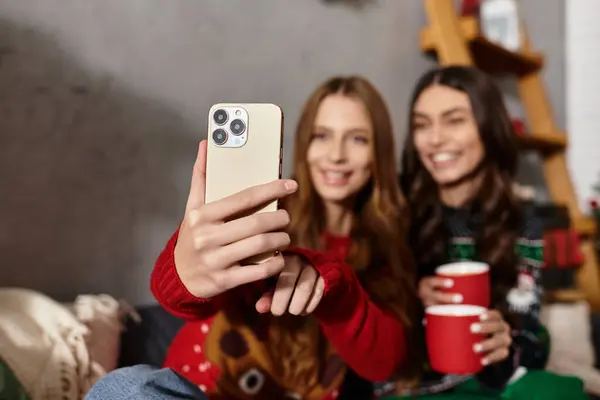 Two girlfriends in cozy sweaters enjoy celebrating Christmas and the New Year together in a warm living room. — Stock Photo
