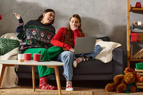 Dos amigas en suéteres festivos disfrutan de un momento alegre juntas en casa, celebrando las fiestas alegremente. - foto de stock