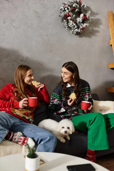 Two girlfriends enjoy festive treats and warm drinks while celebrating Christmas with their dog. — Stock Photo