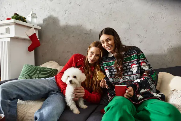 Two girlfriends in cozy sweaters enjoy the holidays with their adorable Bichon Frise, sharing joy and warmth. — Stock Photo
