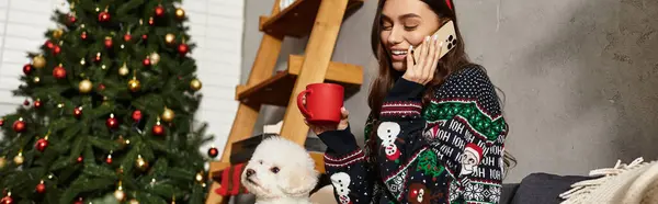 Una giovane donna gode di feste di Capodanno a casa, sorseggiando tè e celebrando con il suo simpatico cane vicino all'albero — Foto stock