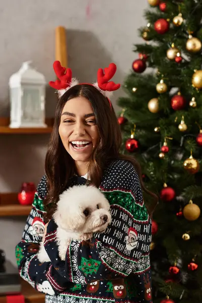 A young woman in a festive sweater shares a joyful moment with her Bichon frise during the holidays. — Stockfoto