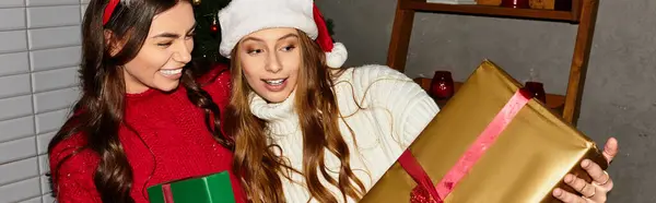 Girlfriends in cozy winter attire share laughter and excitement while unwrapping gifts together. — Stock Photo