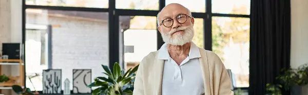 A bearded senior businessman confidently engages in work within a modern office space. — Stock Photo