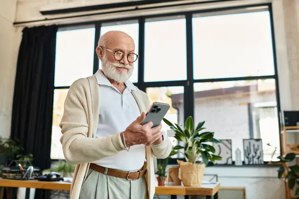 A distinguished senior man with a beard reviews his smartphone, immersed in work at a contemporary office. — Stock Photo
