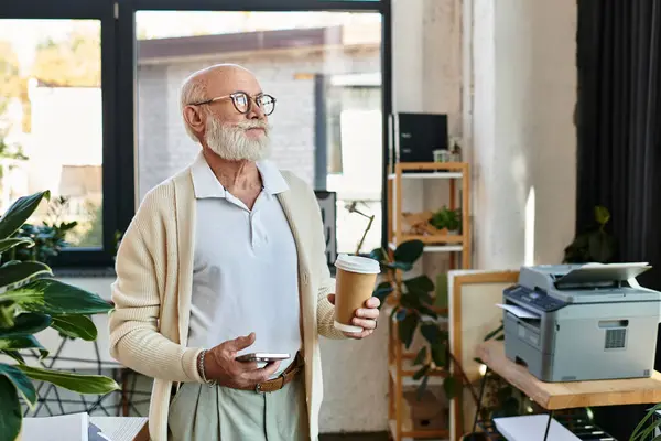 A well-dressed senior businessman holds a coffee cup and smartphone, contemplating ideas in a bright office. — Stock Photo