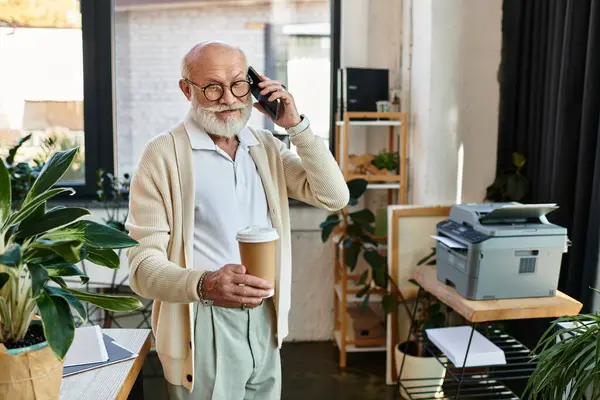 A good-looking senior manager in smart casual attire chats on the phone, coffee in hand, in a stylish office. — Stock Photo