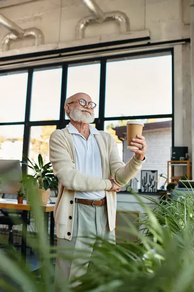 In a contemporary office setting, a senior businessman holds a coffee cup, exuding confidence and style. — Stock Photo