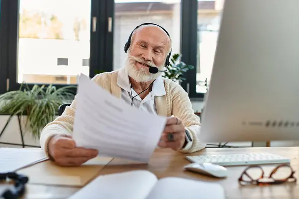 Un uomo d'affari anziano fiducioso sta rivedendo i documenti mentre lavora in remoto in un ambiente di ufficio elegante. — Foto stock