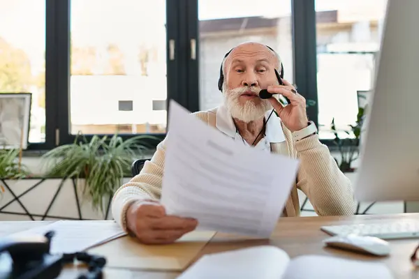 A senior businessman wearing smart casual clothes is actively participating in a conference call, reviewing documents. — Stock Photo