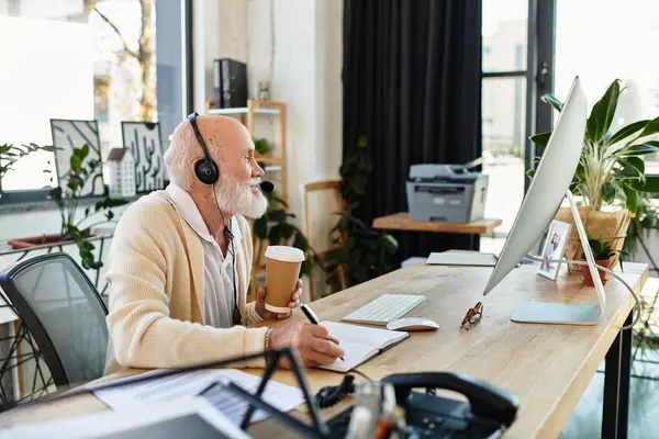 Un bel homme d'affaires senior écoute attentivement lors d'un appel vidéo tout en prenant des notes dans un bureau élégant. — Photo de stock