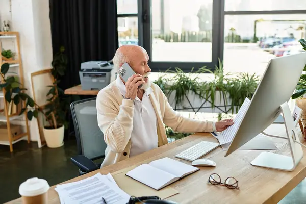A good-looking senior businessman with a beard is actively discussing on his phone while working. — Stock Photo