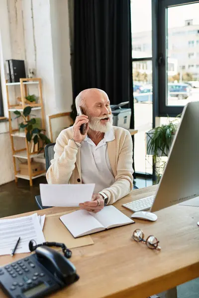 Un illustre professionista anziano comunica su una chiamata mentre lavora alla sua elegante scrivania. — Foto stock