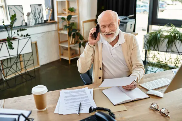 An experienced businessman with a beard speaks on the phone while reviewing important documents at work. — Photo de stock