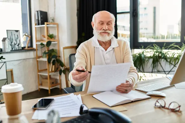 A distinguished senior businessman in smart casual attire carefully reviews papers in a bright office. — Stock Photo