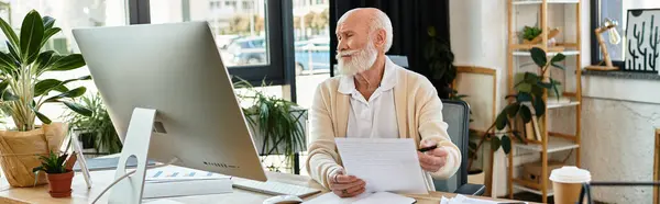 A senior businessman in smart casual attire thoughtfully examines papers at his desk in a stylish office. — Stock Photo