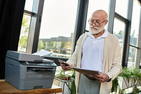 Un uomo d'affari anziano di bell'aspetto controlla il suo telefono mentre gestisce i documenti in un elegante ufficio illuminato dal sole. — Foto stock