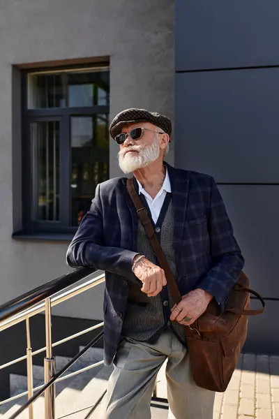 A fashionable senior man with a beard relaxes by a sleek modern building, dressed warmly for autumn. — Stock Photo