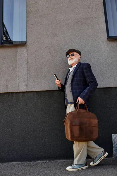 A fashionable senior man strolls confidently near a modern building, dressed in smart casual autumn attire. — Stock Photo