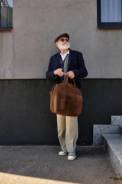 Un signore anziano alla moda si distingue con fiducia da una struttura moderna, in mostra stile autunno con stile. — Foto stock