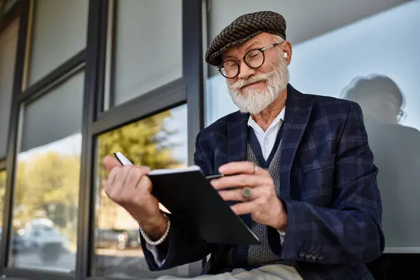 A well-dressed older gentleman is seated outside, jotting down thoughts in a notebook during autumn. — Stock Photo