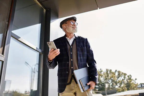 A fashionable senior man holds a phone and notebook, embodying autumn style outside a contemporary structure. — Stock Photo