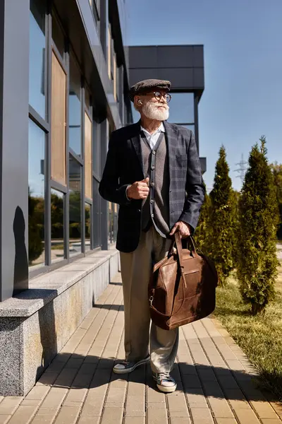 Un homme âgé dans un blazer chic et casquette plate se promène en toute confiance devant un bâtiment moderne en automne. — Photo de stock