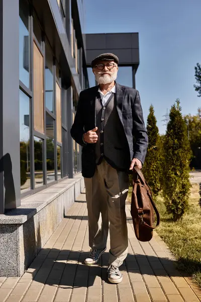 A fashionable senior man strolls confidently by a contemporary building in autumn attire, exuding charm. — Stock Photo