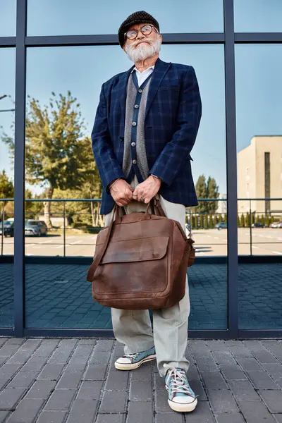 Un elegante signore anziano si erge fiducioso da una struttura contemporanea, trasudando fascino autunno. — Foto stock