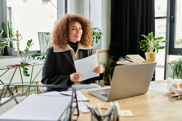A woman smiles while holding papers at her desk surrounded by greenery and sunlight. — Stock Photo