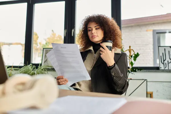 In a cozy and bright workspace, a woman savor her coffee while examining important papers. — Stock Photo