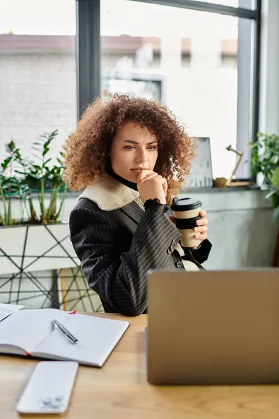 A young woman reflects deeply while sipping coffee in her stylish workspace. — Stock Photo