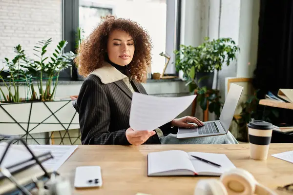 Une femme déterminée lit des papiers assis à son bureau, entouré de plantes et de lumière du soleil.. — Photo de stock
