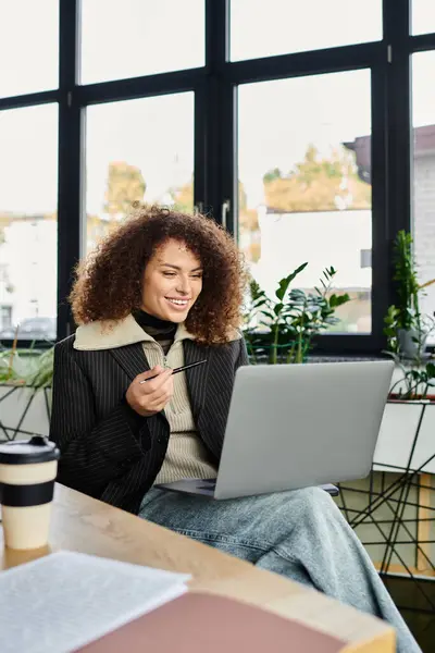 A woman with curly hair smiles as she participates in an online discussion, laptop open. — Stock Photo