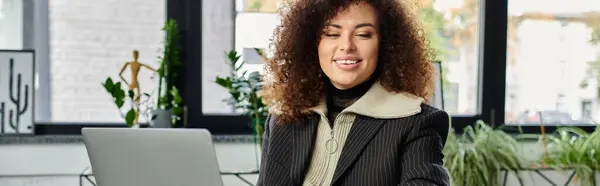 The woman engages with her laptop, smiling in a cozy, plant filled workspace. — Stock Photo