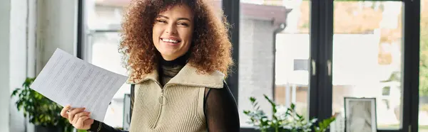 A joyful woman smiles brightly while presenting important papers in a sunny office. — Stock Photo