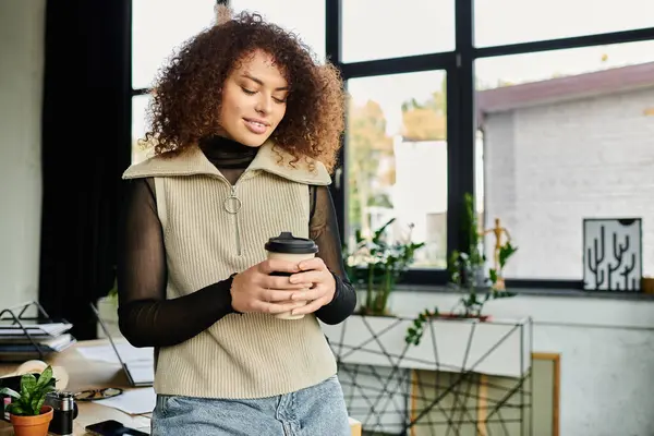A woman in a stylish outfit smiles while holding a cup of coffee in her serene workspace. — Stock Photo