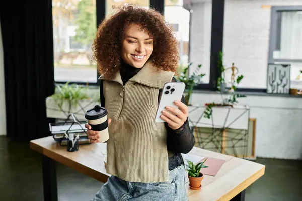 Cheerful woman smiling at her smartphone with coffee in hand in office. — Stock Photo