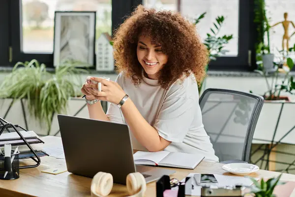 A woman smiles with a coffee cup, concentrating on work at her colorful home office desk. — Stock Photo