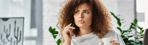 A woman sits thoughtfully in a stylish office, holding a warm drink as she contemplates ideas. — Stock Photo