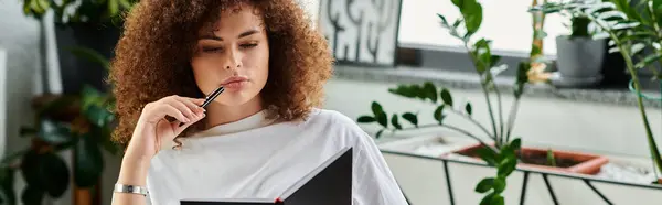 A woman ponders deeply as she writes in her notebook, immersed in a tranquil indoor garden. — Stockfoto