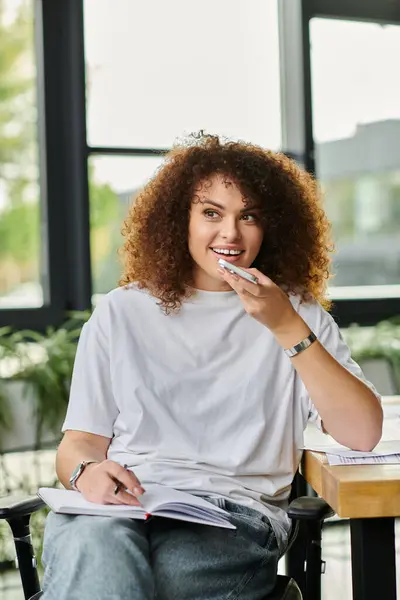 A woman with curly hair sits comfortably, reflecting thoughtfully while studying diligently. — Stock Photo