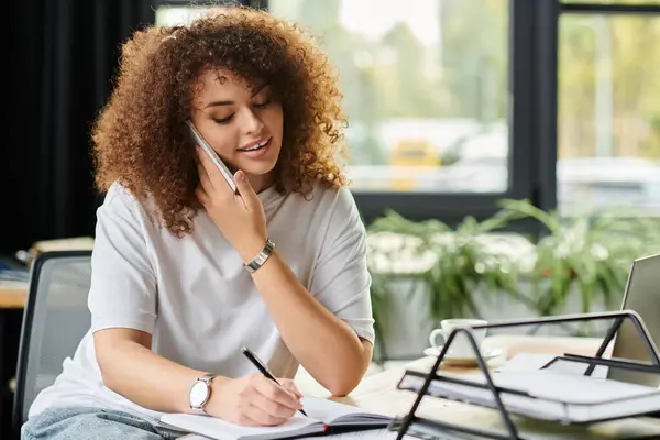 The young woman types on her phone and scribbles ideas in a notebook, enjoying her space. — Stock Photo