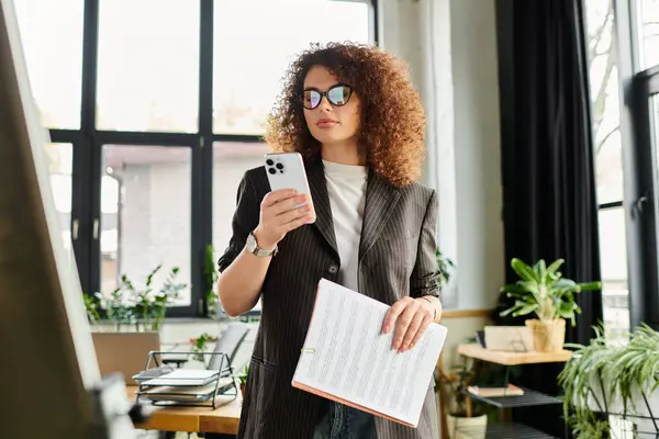 The woman thoughtfully checks her smartphone while holding documents, surrounded by greenery. — Stock Photo