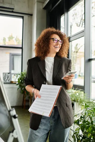 The woman confidently holds a smartphone and documents while sharing a joyful moment. — Stock Photo