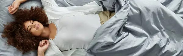 The woman relaxes peacefully in bed, surrounded by soft bedding. — Stock Photo
