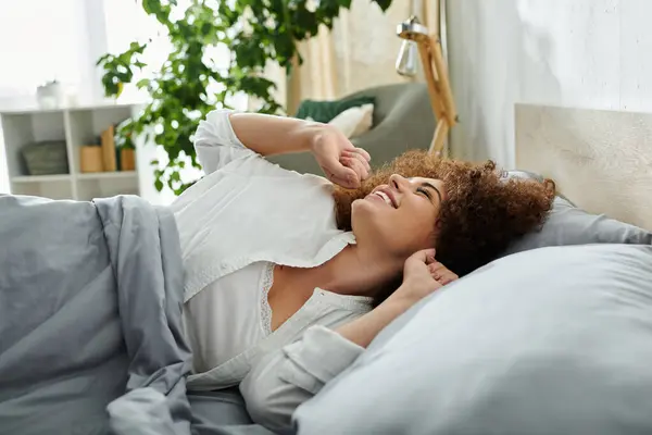 A cheerful woman awakens and stretches in her soft bed, surrounded by a peaceful ambiance. — Stock Photo
