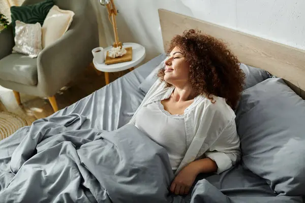 A woman lounges peacefully on her bed, surrounded by a cozy atmosphere and soft textiles. — Stock Photo