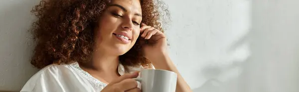 Una donna si rilassa e sorride dolcemente sorseggiando una bevanda calda alla luce del sole di mezzogiorno. — Foto stock